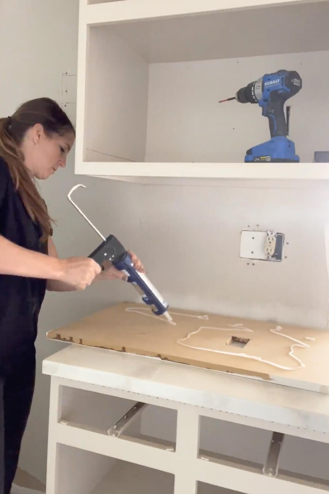 Attaching a faux marble kitchen backsplash using liquid nails.